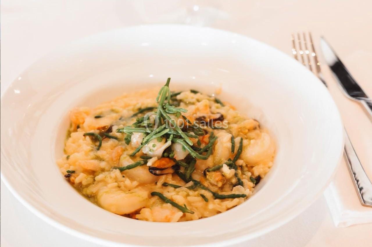 Assiette de risotto crémeux aux fruits de mer, garnie de feuilles de basilic frais, servie sur une table blanche.