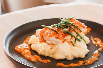 Salle de restaurant lumineuse avec tables dressées, chaises rembourrées, mur décoré de bouteilles de vin et lustre suspendu.