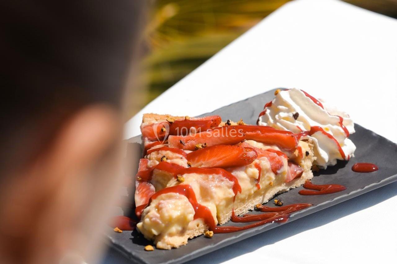 Part de tarte aux fraises avec crème fouettée et coulis rouge, servie sur une assiette noire.