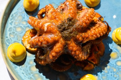 Salle de restaurant lumineuse avec tables dressées, chaises rembourrées, mur décoré de bouteilles de vin et lustre suspendu.