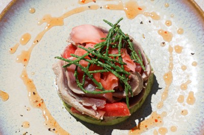 Salle de restaurant lumineuse avec tables dressées, chaises rembourrées, mur décoré de bouteilles de vin et lustre suspendu.