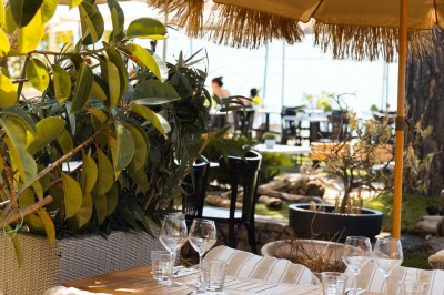 Salle de restaurant lumineuse avec tables dressées, chaises rembourrées, mur décoré de bouteilles de vin et lustre suspendu.