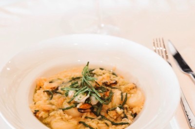 Salle de restaurant lumineuse avec tables dressées, chaises rembourrées, mur décoré de bouteilles de vin et lustre suspendu.