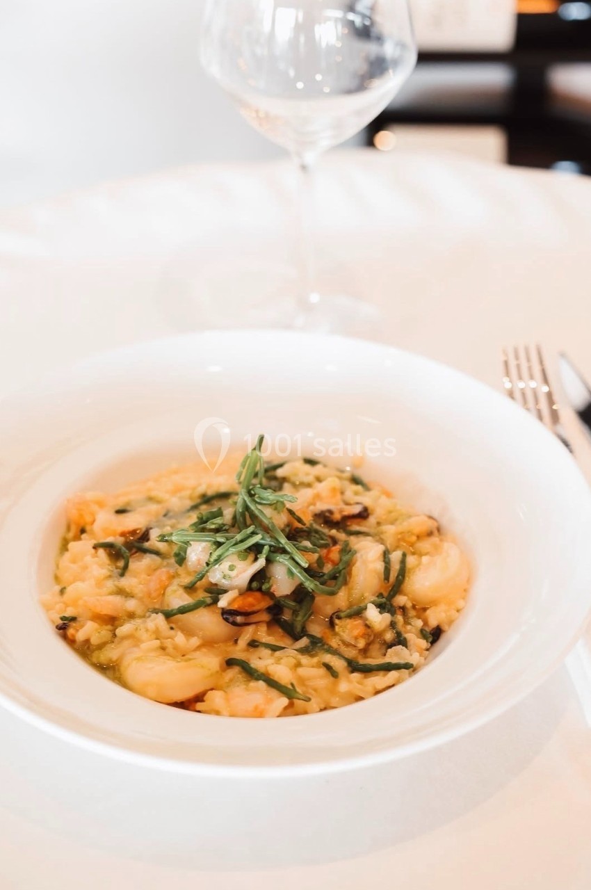 Assiette de risotto crémeux aux crevettes et herbes fraîches, servie sur une table avec couverts et verre à vin.