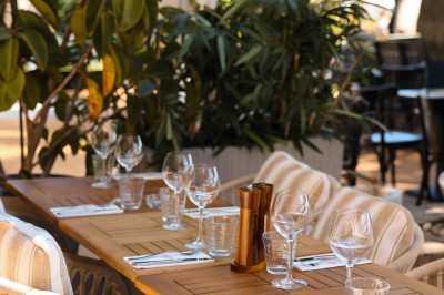 Salle de restaurant lumineuse avec tables dressées, chaises rembourrées, mur décoré de bouteilles de vin et lustre suspendu.