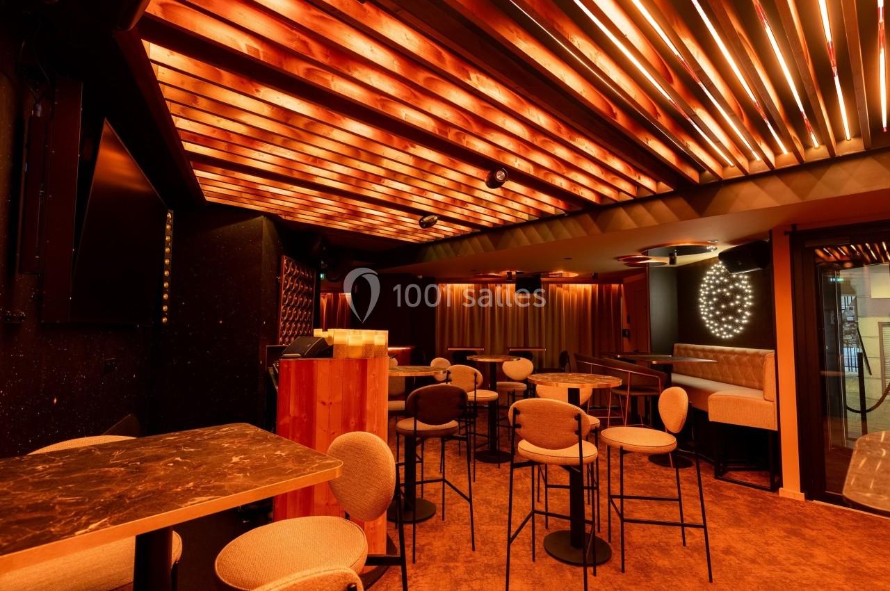 Salle moderne avec éclairage chaleureux, plafond en bois, tables hautes, chaises rembourrées et ambiance intimiste.