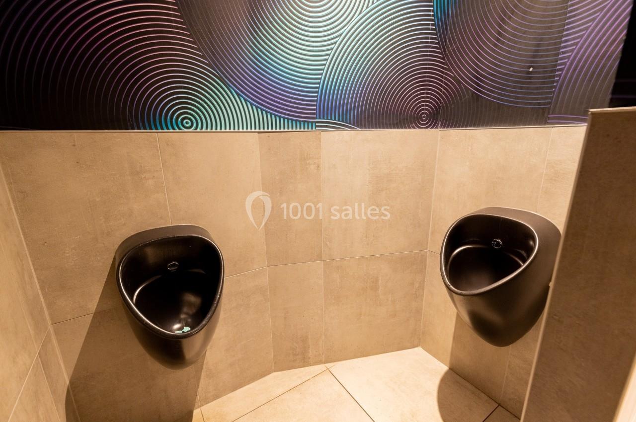 Deux urinoirs noirs fixés à un mur carrelé beige, avec un décor mural aux motifs circulaires colorés.