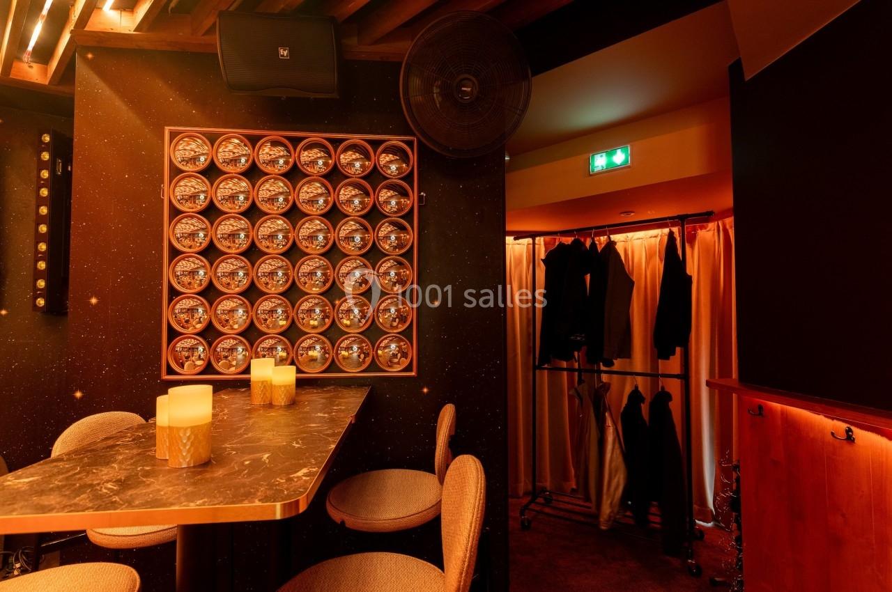 Table en marbre avec bougies, chaises rembourrées, mur décoré de cercles lumineux, portant à vêtements en arrière-plan.