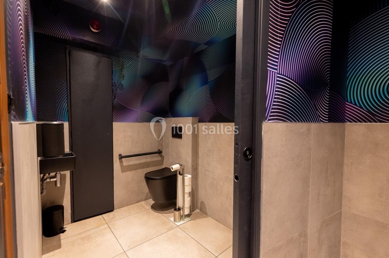 Toilettes modernes avec murs décorés de motifs géométriques colorés, sol carrelé et équipements noirs.