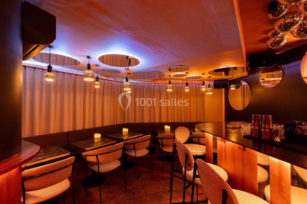 Salle de restaurant avec éclairage tamisé, tables en bois sombre, chaises rembourrées et décorations modernes.