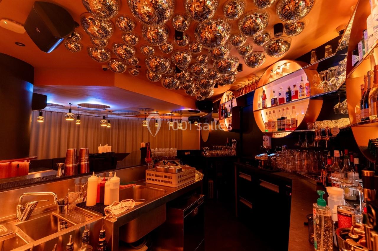 Intérieur d'un bar avec un plafond décoré de boules miroir, éclairage tamisé et comptoir équipé pour les cocktails.