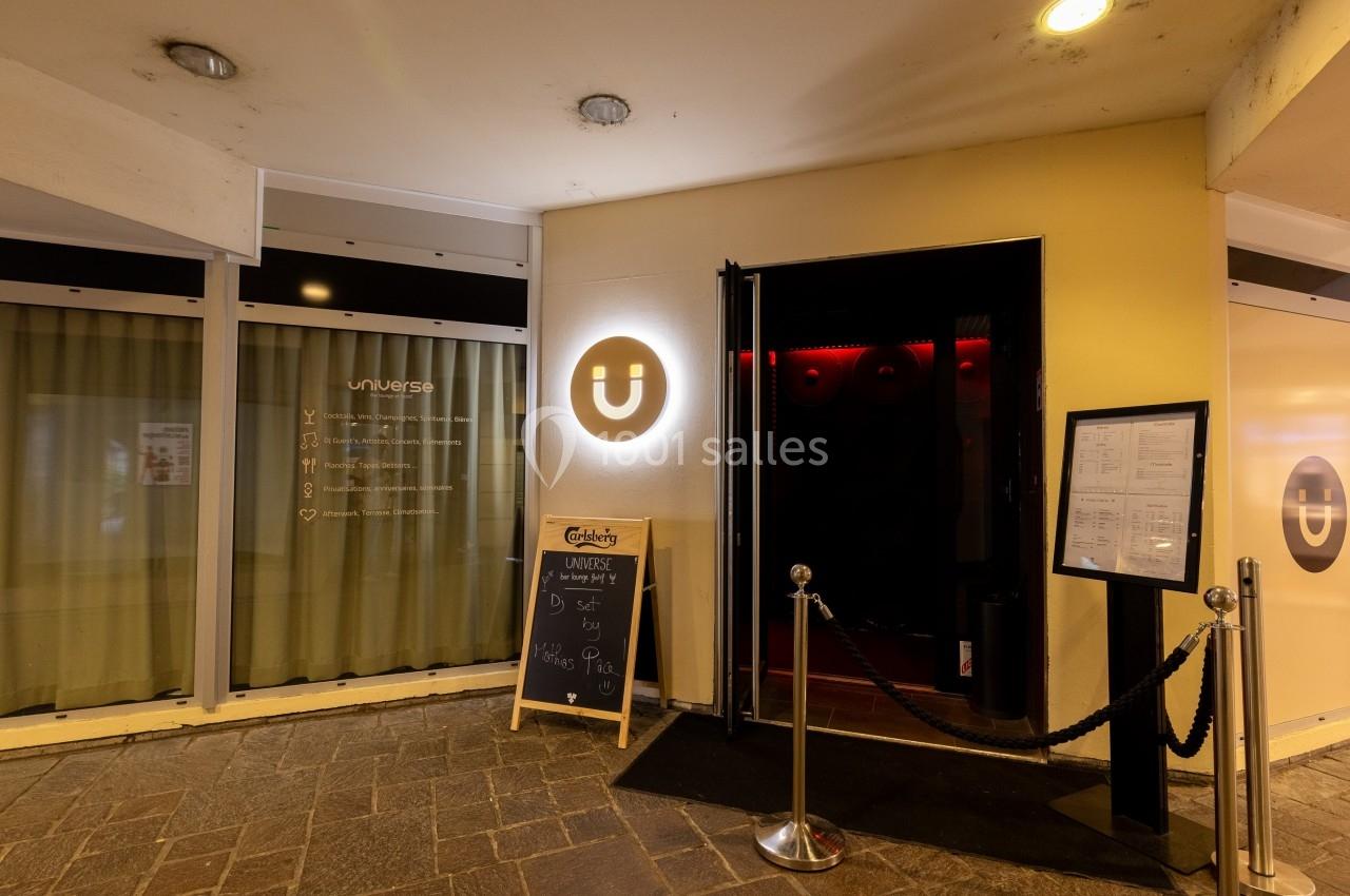 Entrée d'un établissement avec un logo lumineux en forme de U, un tableau noir et une carte affichée à l'extérieur.