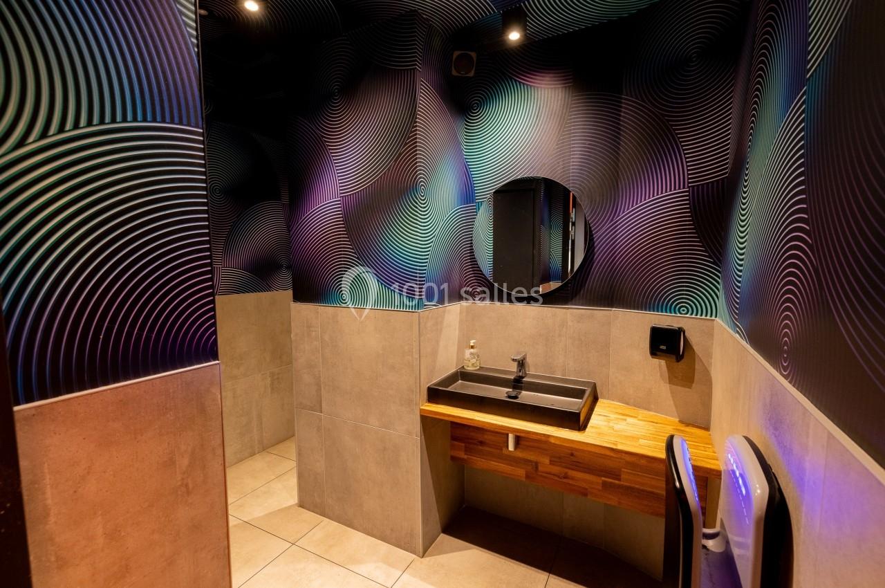 Salle de bain moderne avec lavabo sur plan en bois, miroir rond et murs décorés de motifs géométriques colorés.