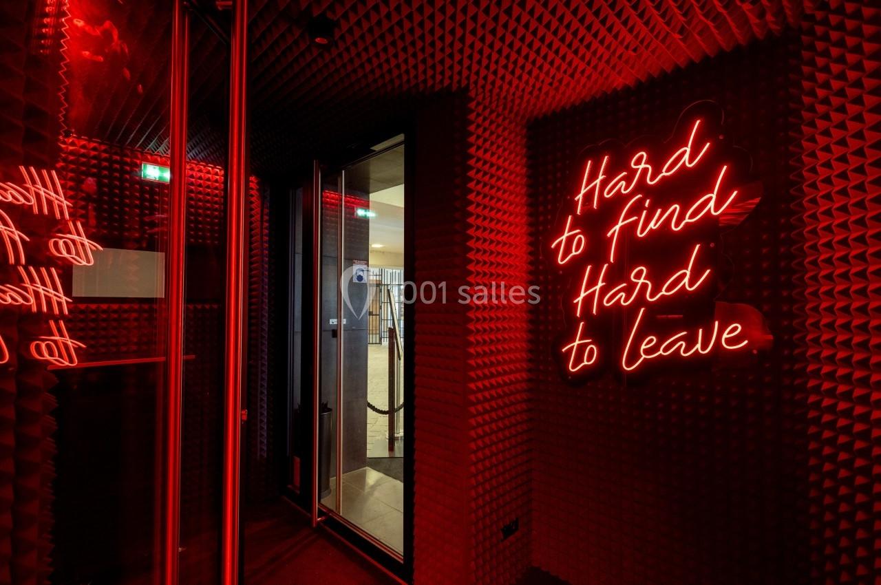Mur recouvert de panneaux acoustiques rouges avec une enseigne néon indiquant ’Hard to find, Hard to leave’.