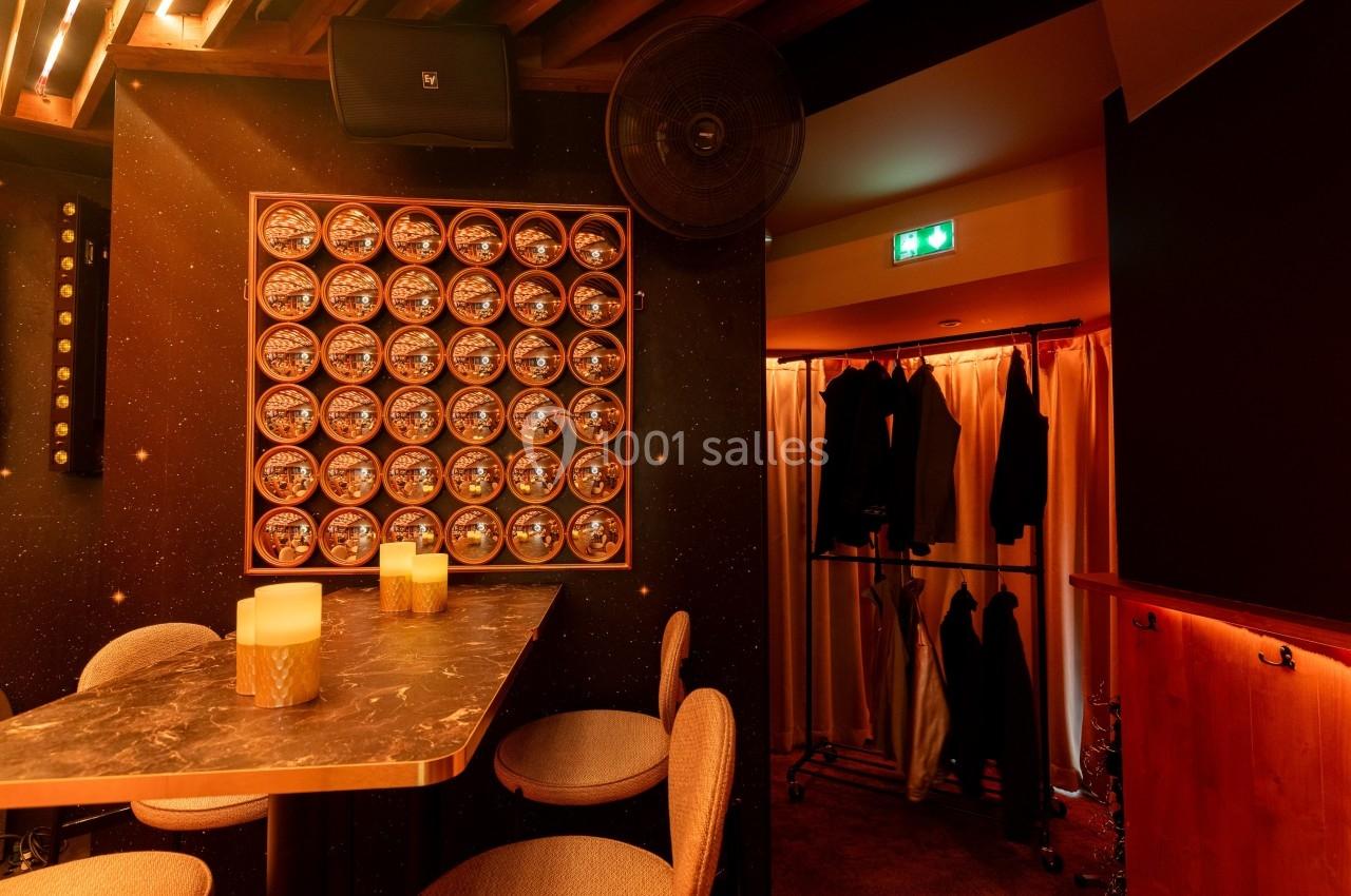 Table en marbre avec bougies, chaises rembourrées, mur décoré de cercles lumineux, portant à vêtements en arrière-plan.