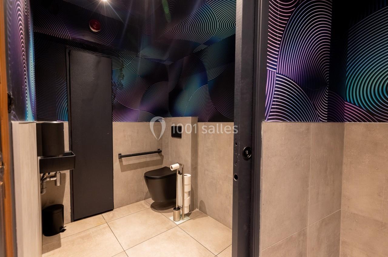 Toilettes modernes avec murs décorés de motifs géométriques colorés, sol en carrelage beige et équipements noirs.