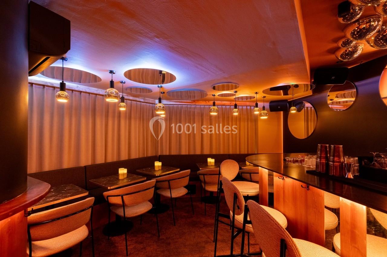 Salle de restaurant avec éclairage tamisé, tables en bois, chaises rembourrées et rideaux beige en arrière-plan.