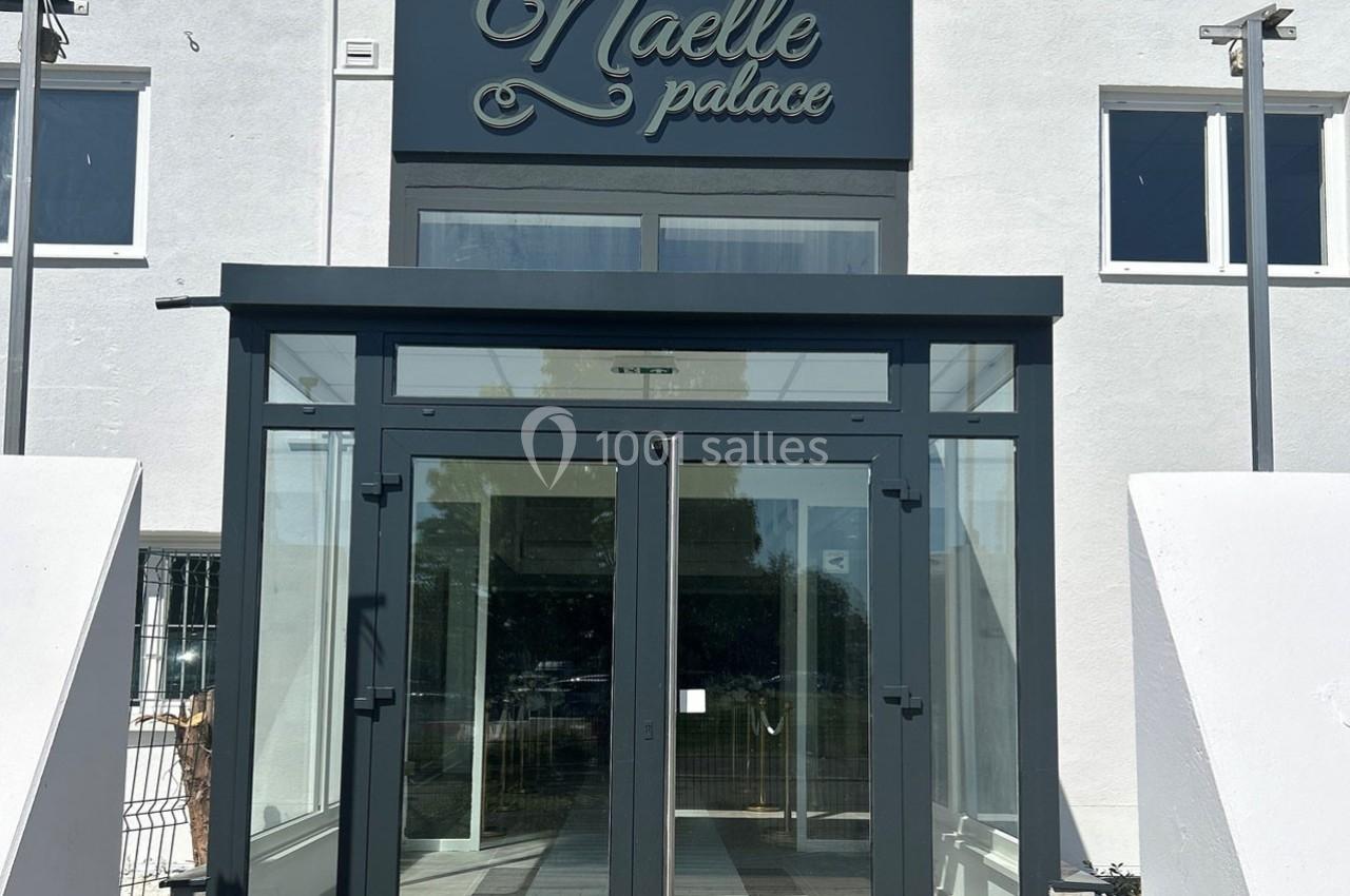 Entrée vitrée moderne d'un bâtiment avec une enseigne ’Naelle Palace’ sur la façade blanche.