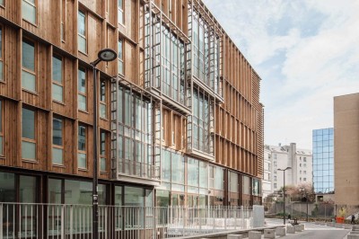 Façade d'un immeuble moderne en bois et verre avec des fenêtres alignées, situé dans un environnement urbain.