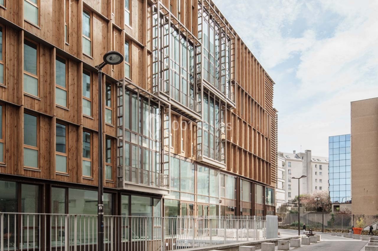 Façade d'un immeuble moderne en bois et verre avec des fenêtres alignées, situé dans un environnement urbain.