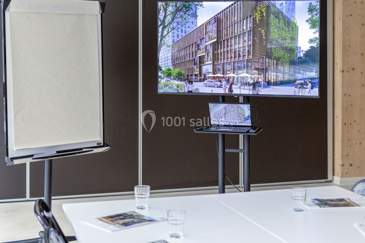Écran affichant un projet architectural dans une salle de réunion équipée d'un paperboard et de tables avec documents.
