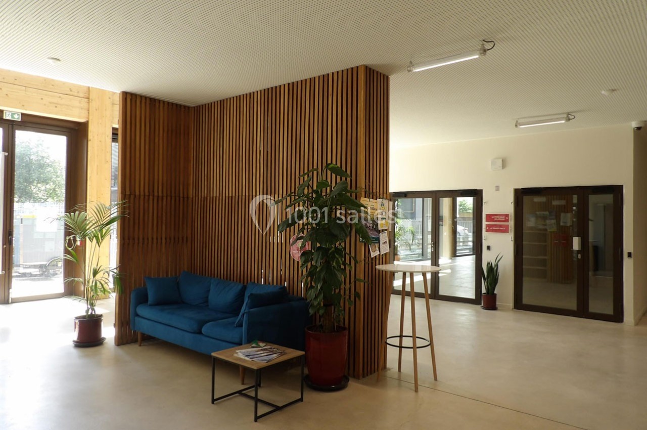 Espace d'accueil lumineux avec canapé bleu, plantes en pot, table haute et paroi en bois ajouré.