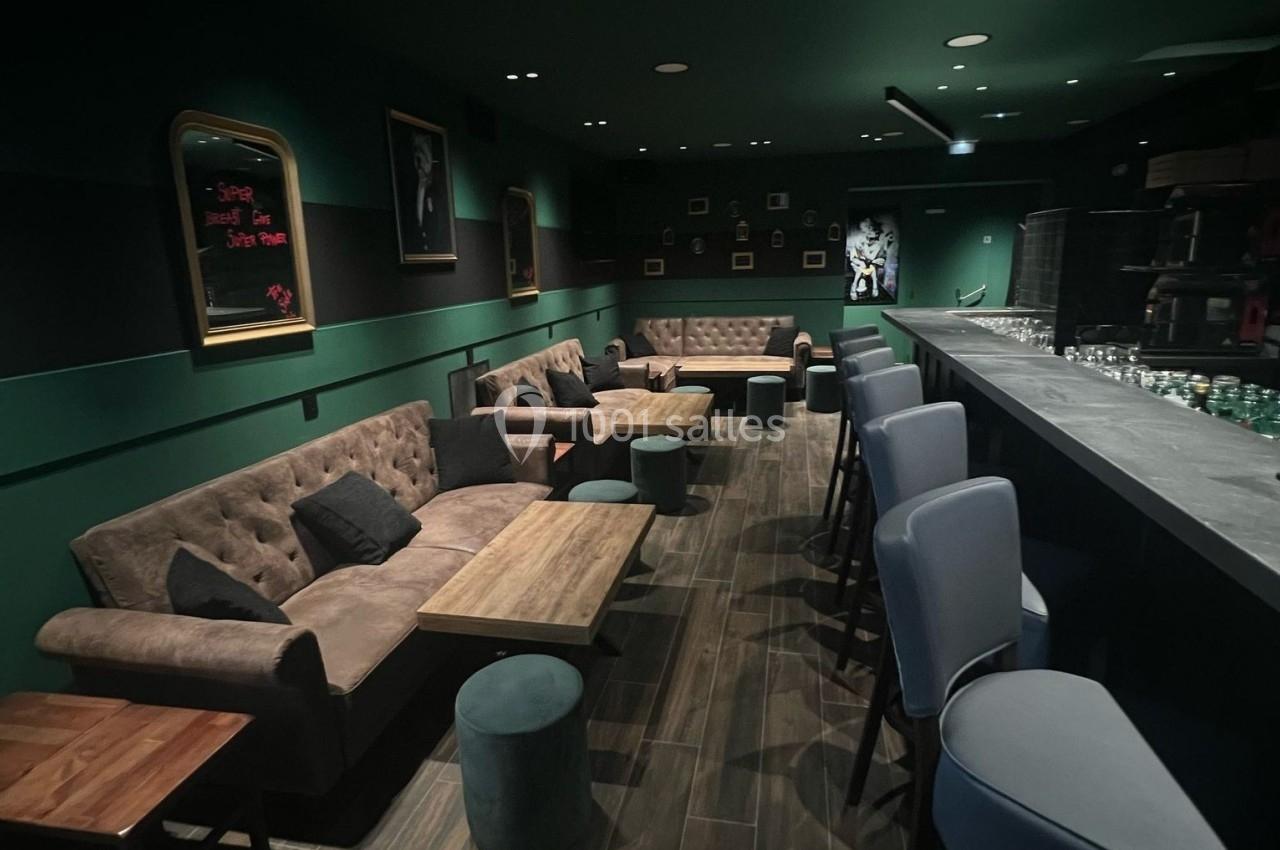Salle de bar moderne avec canapés, tables basses en bois, tabourets et éclairage tamisé.