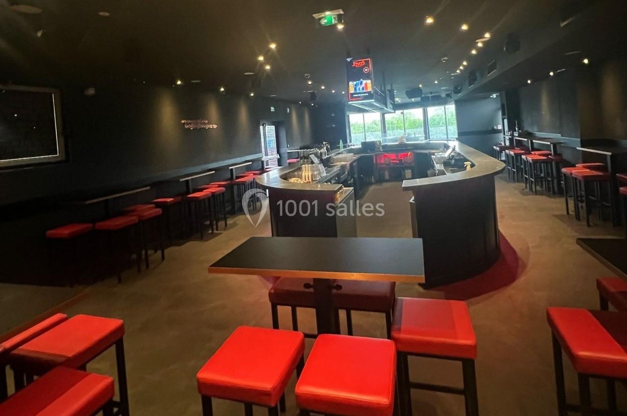 Salle de bar moderne avec comptoir central, tabourets rouges et éclairage tamisé.