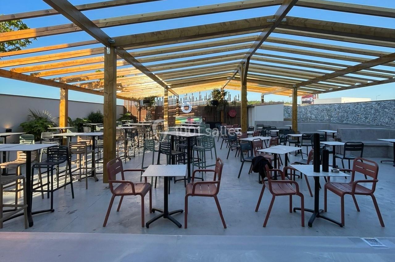 Terrasse extérieure couverte avec des tables et des chaises disposées sous une structure en bois clair.