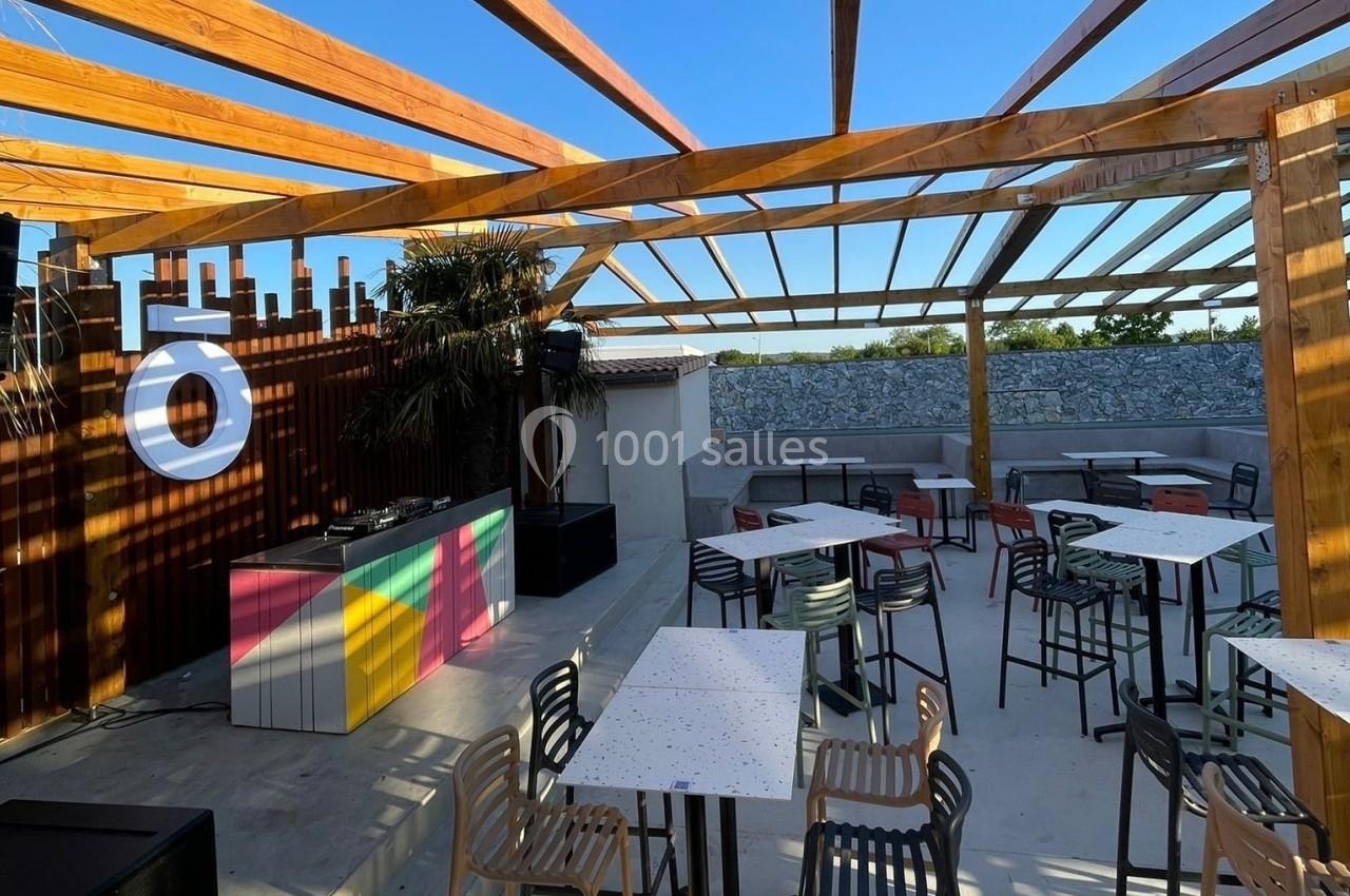 Terrasse en plein air avec pergola en bois, tables, chaises et un comptoir coloré sous un ciel dégagé.