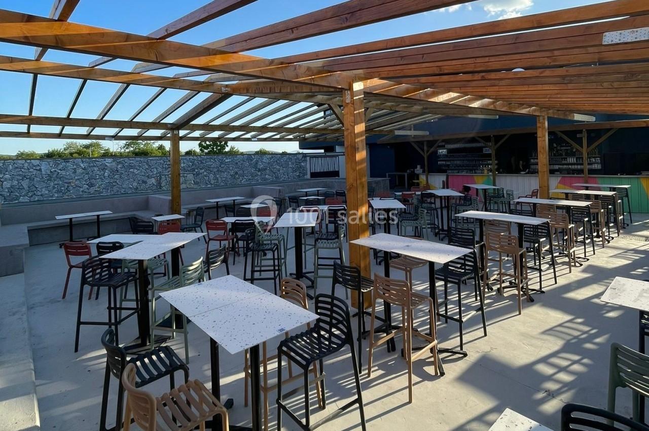 Terrasse extérieure avec tables et chaises sous une pergola en bois, bar en arrière-plan.