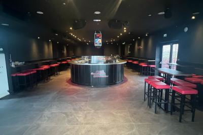 Terrain gravillonné entouré de végétation, avec un bâtiment moderne à droite et un ciel nuageux en arrière-plan.