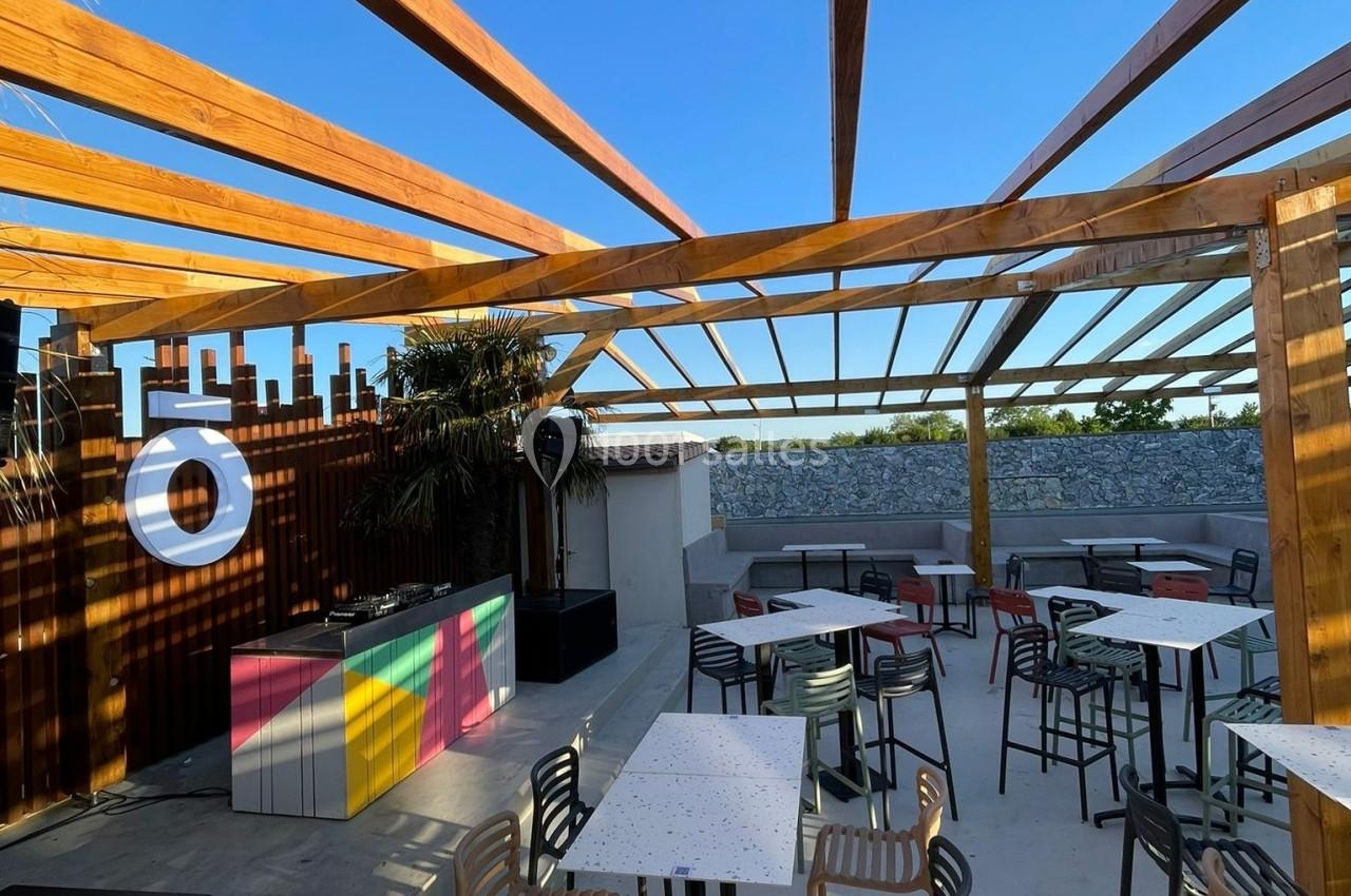 Terrasse extérieure avec tables, chaises et pergola en bois, sous un ciel bleu dégagé.