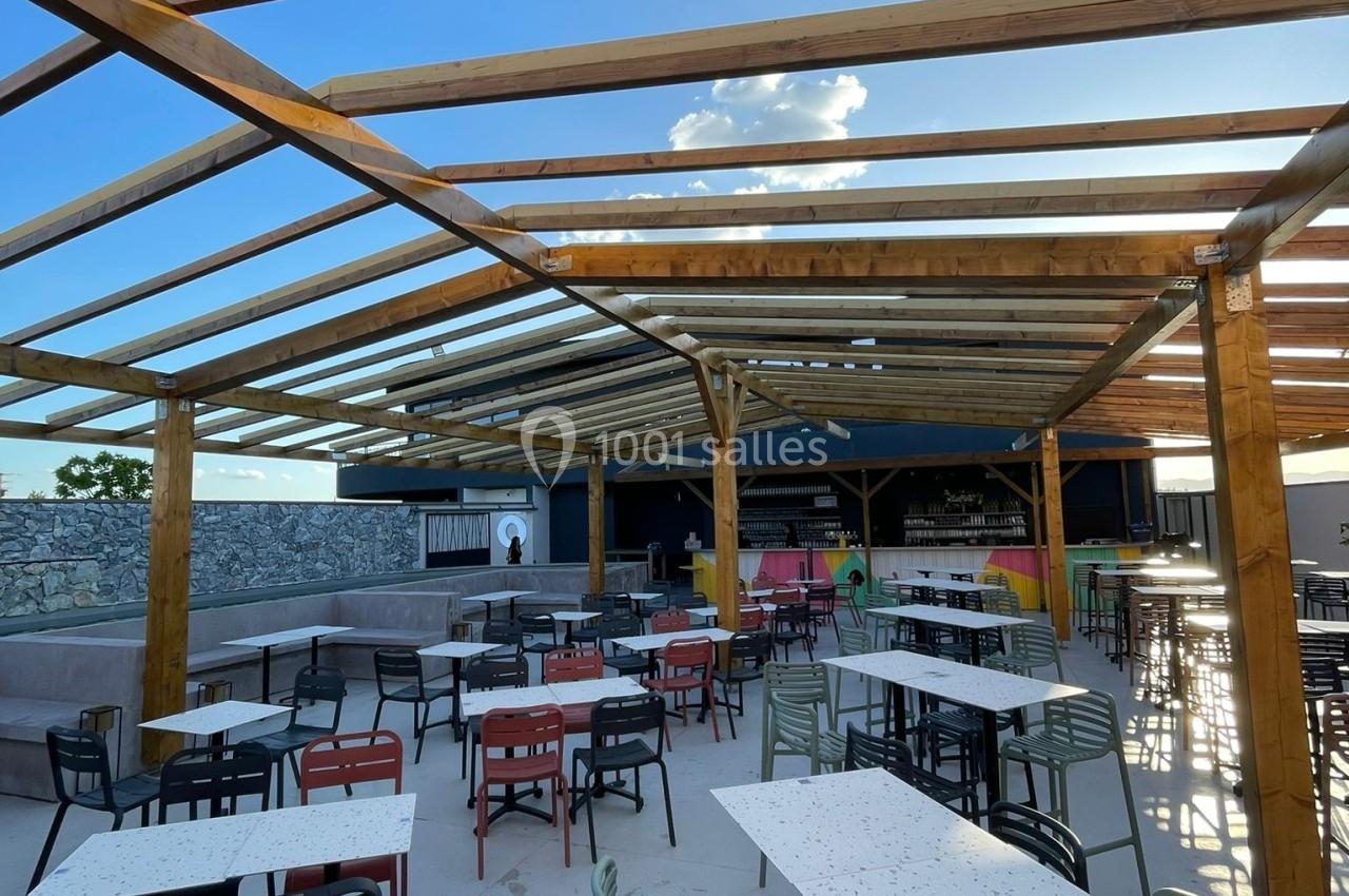Terrasse extérieure avec tables et chaises colorées sous une structure en bois ouverte, ciel bleu en arrière-plan.