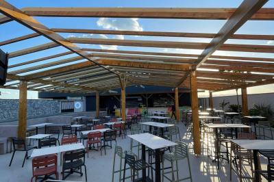 Terrain gravillonné entouré de végétation, avec un bâtiment moderne à droite et un ciel nuageux en arrière-plan.