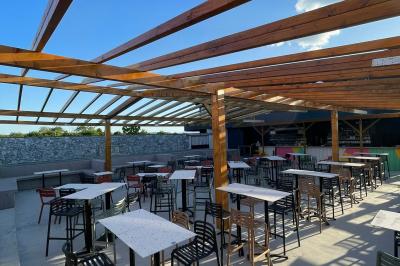 Terrain gravillonné entouré de végétation, avec un bâtiment moderne à droite et un ciel nuageux en arrière-plan.