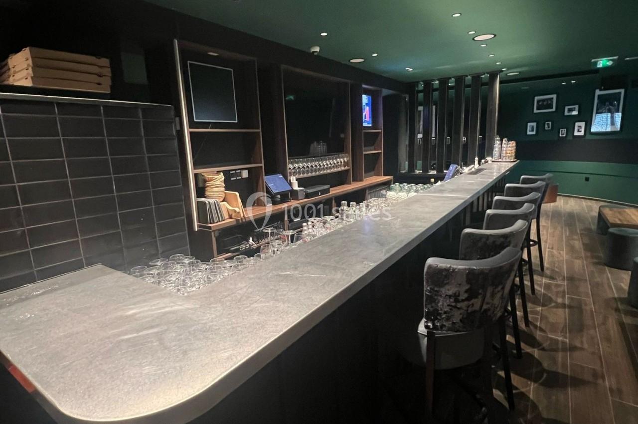 Bar avec comptoir en pierre, tabourets rembourrés, étagères en bois et éclairage tamisé dans une ambiance moderne.