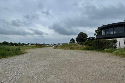 Terrain gravillonné entouré de végétation, avec un bâtiment moderne à droite et un ciel nuageux en arrière-plan.