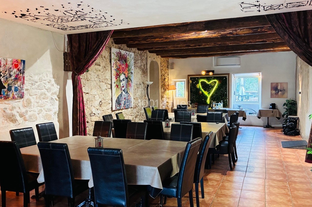 Salle de restaurant avec murs en pierre, poutres apparentes, tableaux colorés et décoration lumineuse en forme de cœur.