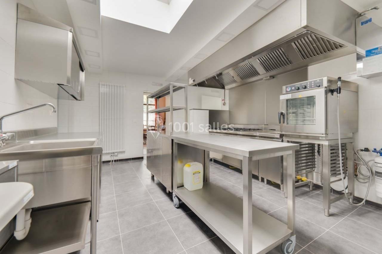 Cuisine professionnelle moderne avec équipements en inox, four, évier et plan de travail sur un sol en carrelage gris.