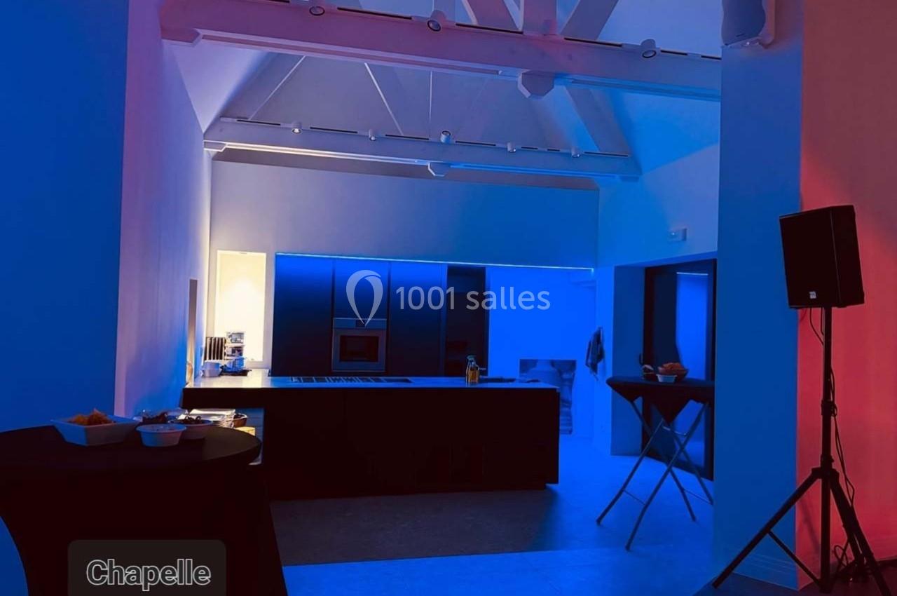 Cuisine moderne éclairée par des lumières bleues et rouges, avec des tables hautes et un plafond à poutres apparentes.