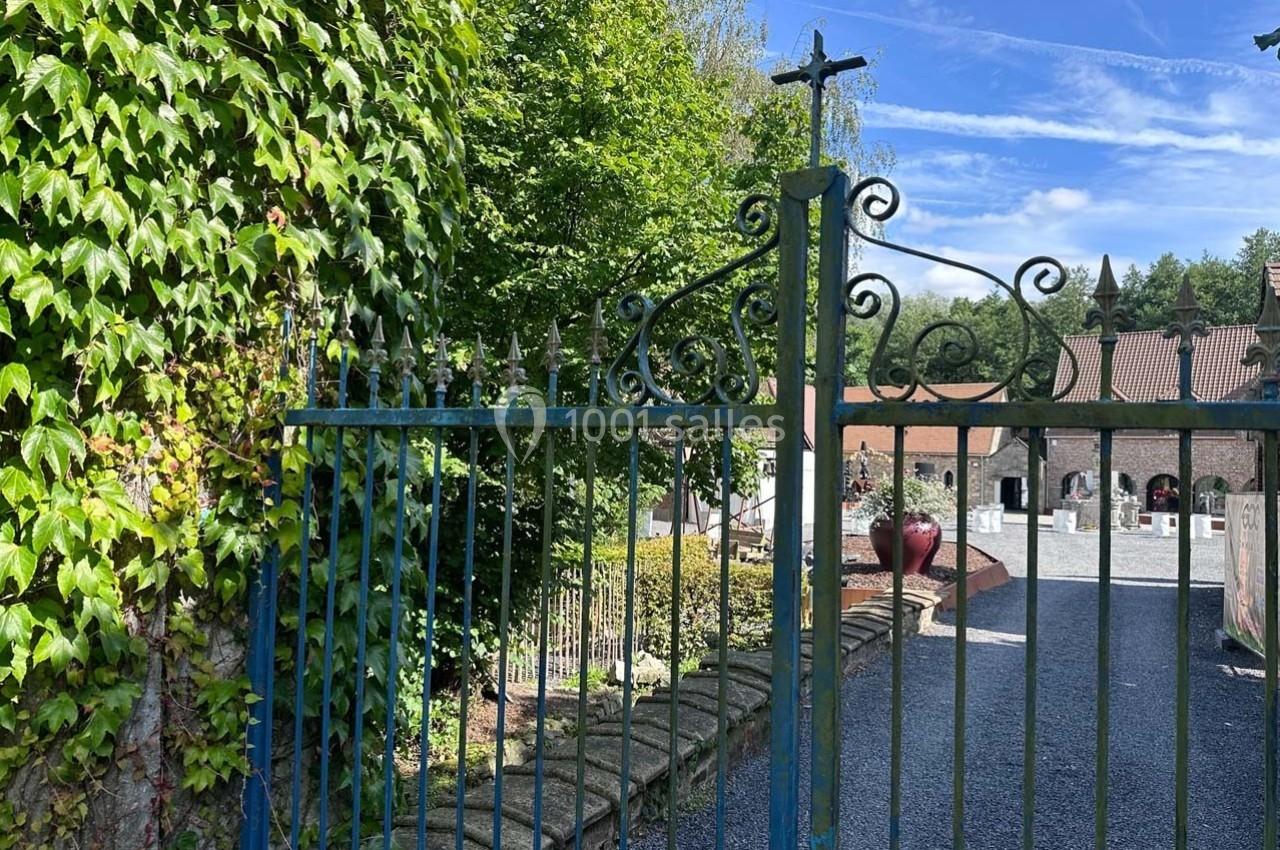 Portail en fer forgé ouvrant sur une allée pavée bordée de verdure, menant à un bâtiment en arrière-plan.