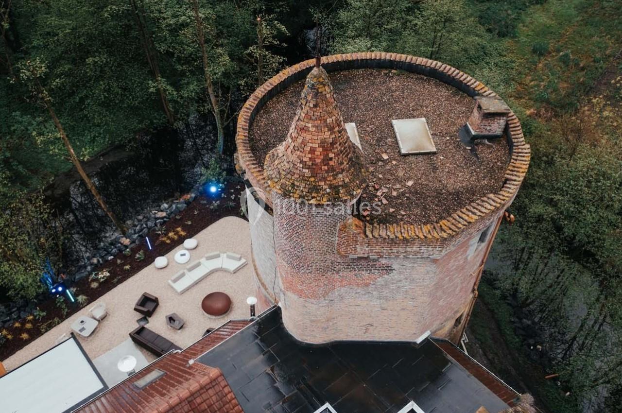 Vue aérienne d'une tour en briques avec un toit conique, entourée de végétation et d'une terrasse aménagée.