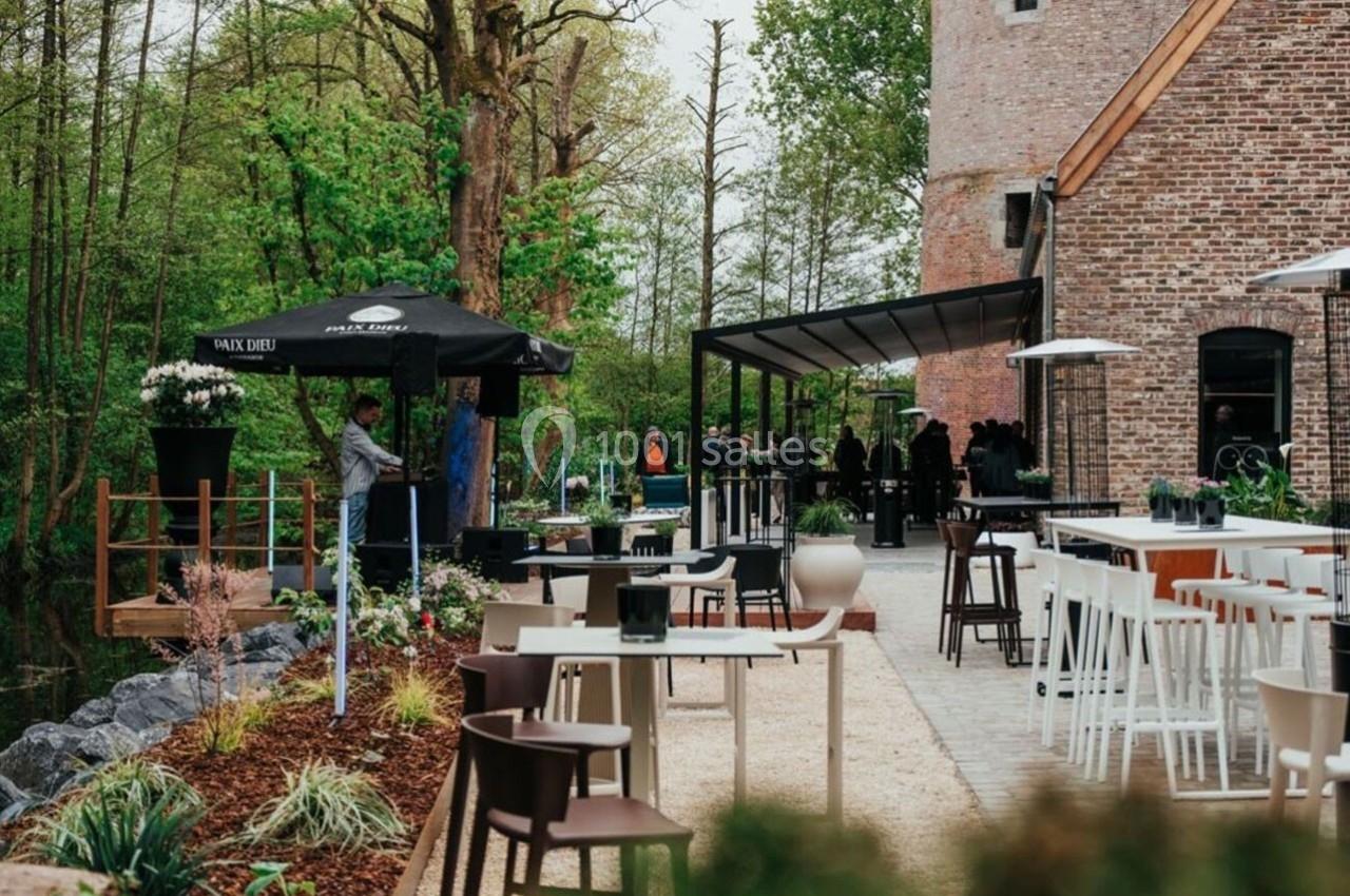 Terrasse extérieure aménagée avec tables et chaises, entourée de verdure et jouxtant un bâtiment en briques.