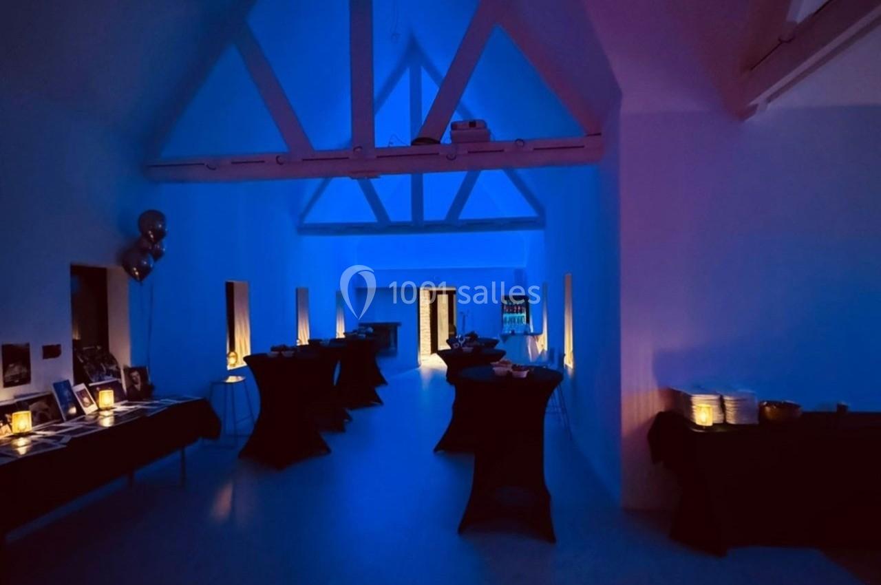 Salle sombre éclairée par une lumière bleue, avec des tables noires disposées le long des murs.
