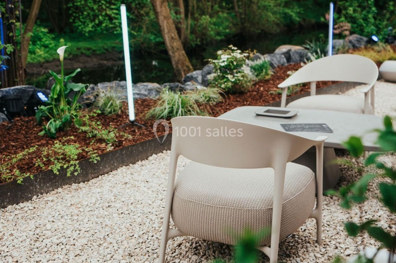 Deux fauteuils beiges et une table basse sur un sol en gravier, entourés de plantes et d'un éclairage extérieur.