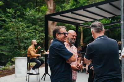 Des personnes discutent debout dans un espace extérieur, entourées de verdure et de mobilier de jardin.