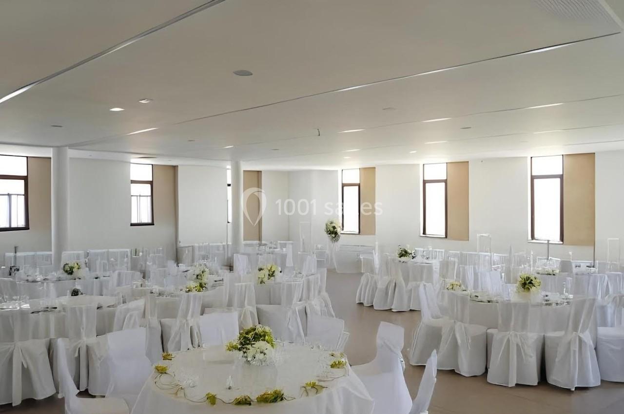 Salle de réception lumineuse avec des tables rondes dressées de nappes blanches et décorées de fleurs.