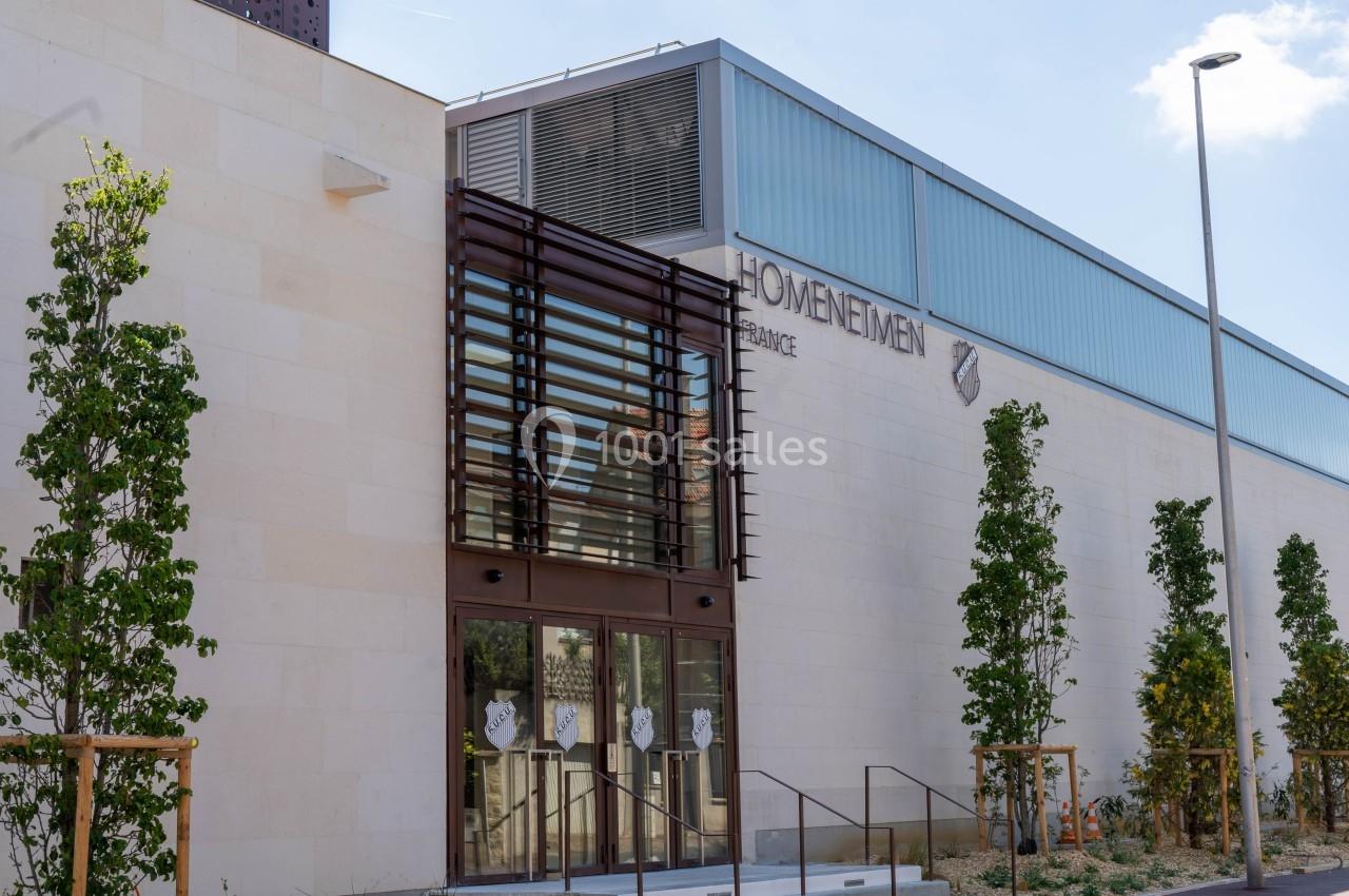 Façade d'un bâtiment moderne en pierre claire avec des arbres plantés devant et une enseigne ’Homenetmen France’.