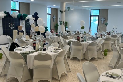 Table ronde dressée pour un événement, avec nappes blanches, serviettes vertes, bougies et boissons disposées au centre.